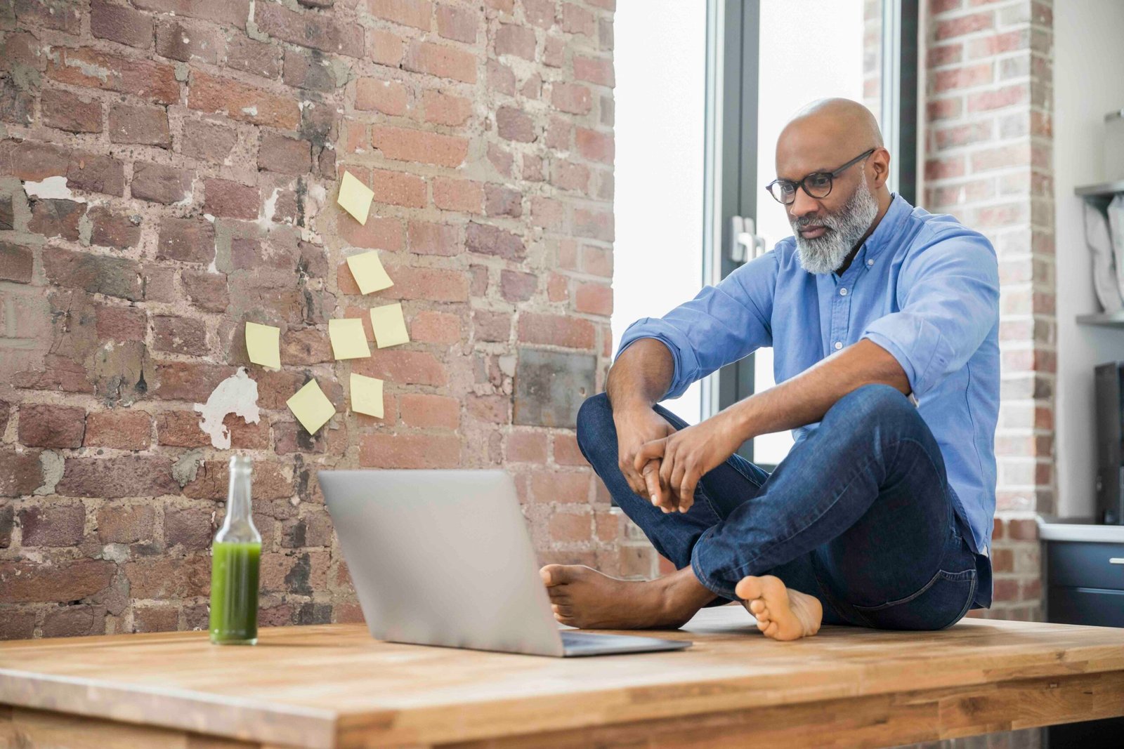 A focused entrepreneur sitting on a table, analyzing user insights on a laptop in a modern office space.